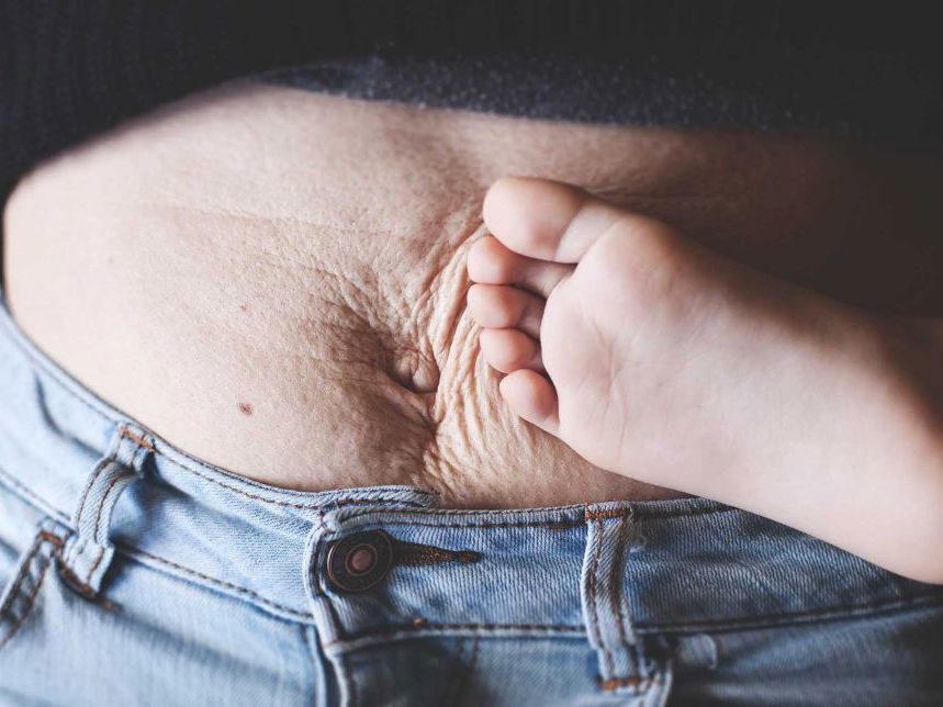 Kinderfuß an faltigem Mama-Bauch.