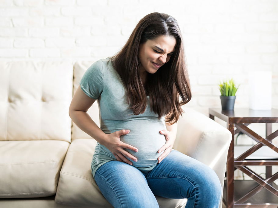 Eine schwangere Frau mit schmerzverzerrtem Gesicht hält ihren Babybauch.