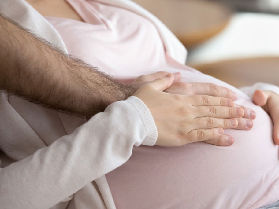 Frau und Mann legen Hände auf Babybauch.