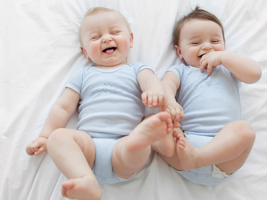 Baby-Zwillinge liegen nebeneinander und lachen.