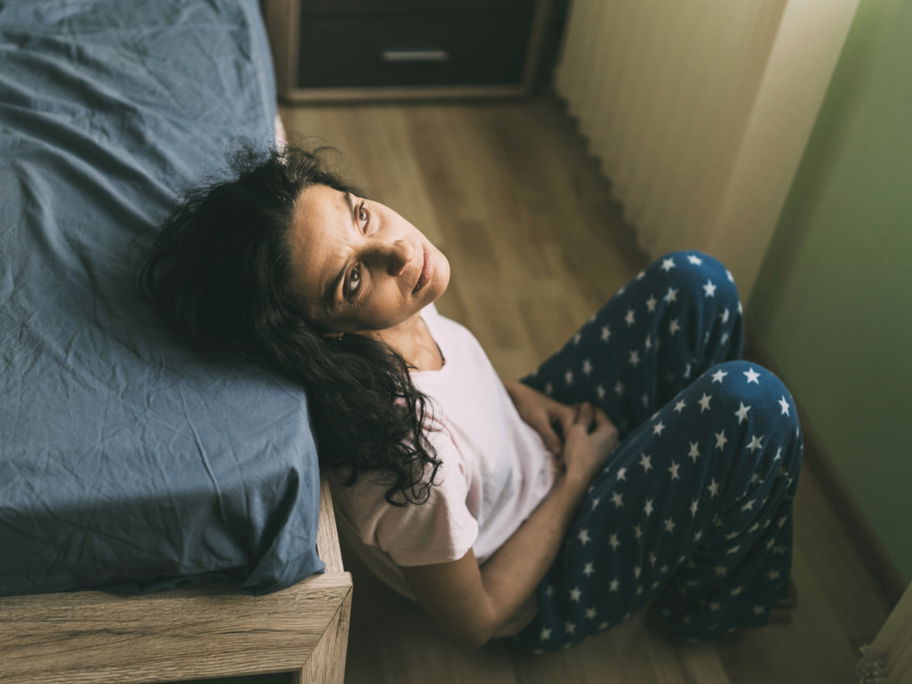 Frau sitzt vorm Bett und starrt an die Decke.