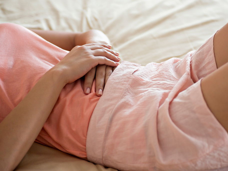 Frau liegt auf dem Bett und hält sich die Hände auf den Bauch.