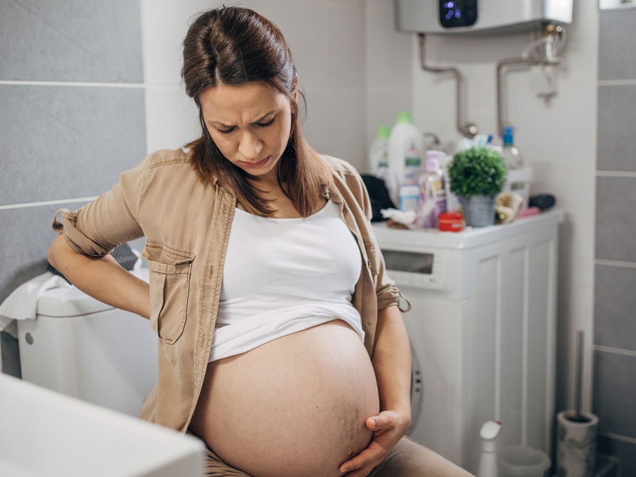 Schwangere Frau mit Schmerzen auf der Toilette.