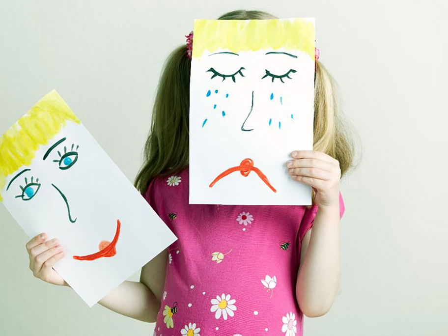 Gefühle zeigen: Kind hält gemaltes, trauriges Gesicht vor ihr eigenes.