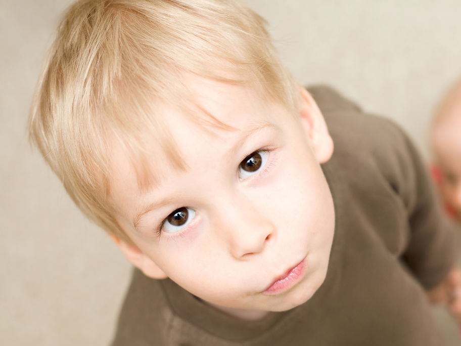 Ein kleiner Junge schaut genervt, während ein Baby sich an ihm hochzieht.